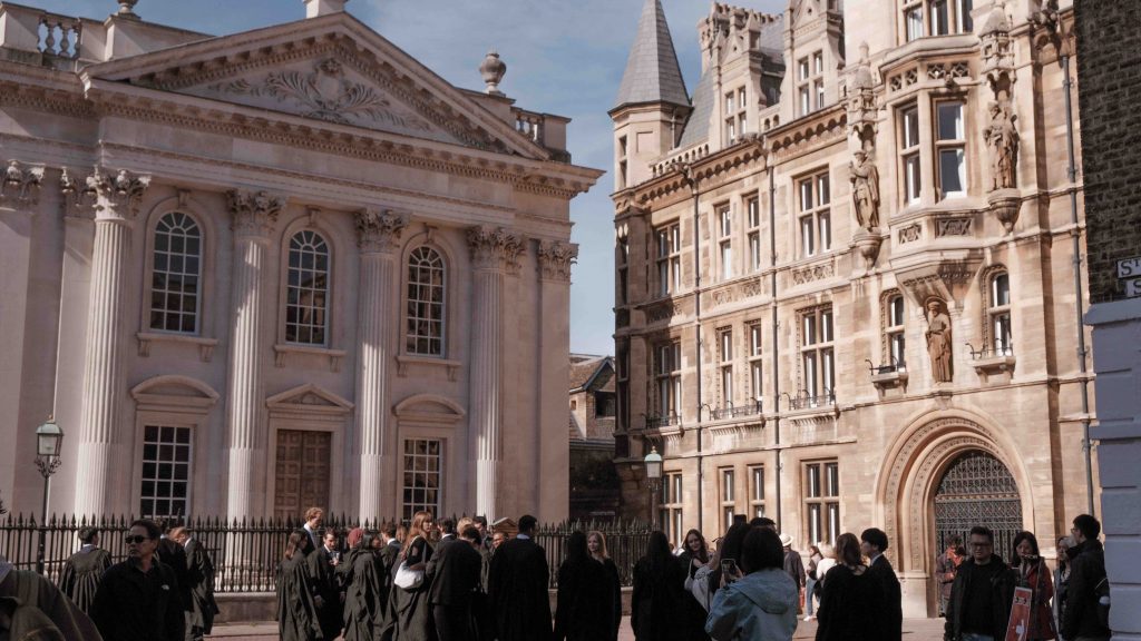 Cambridge students in black gowns standing outside the Senate House building